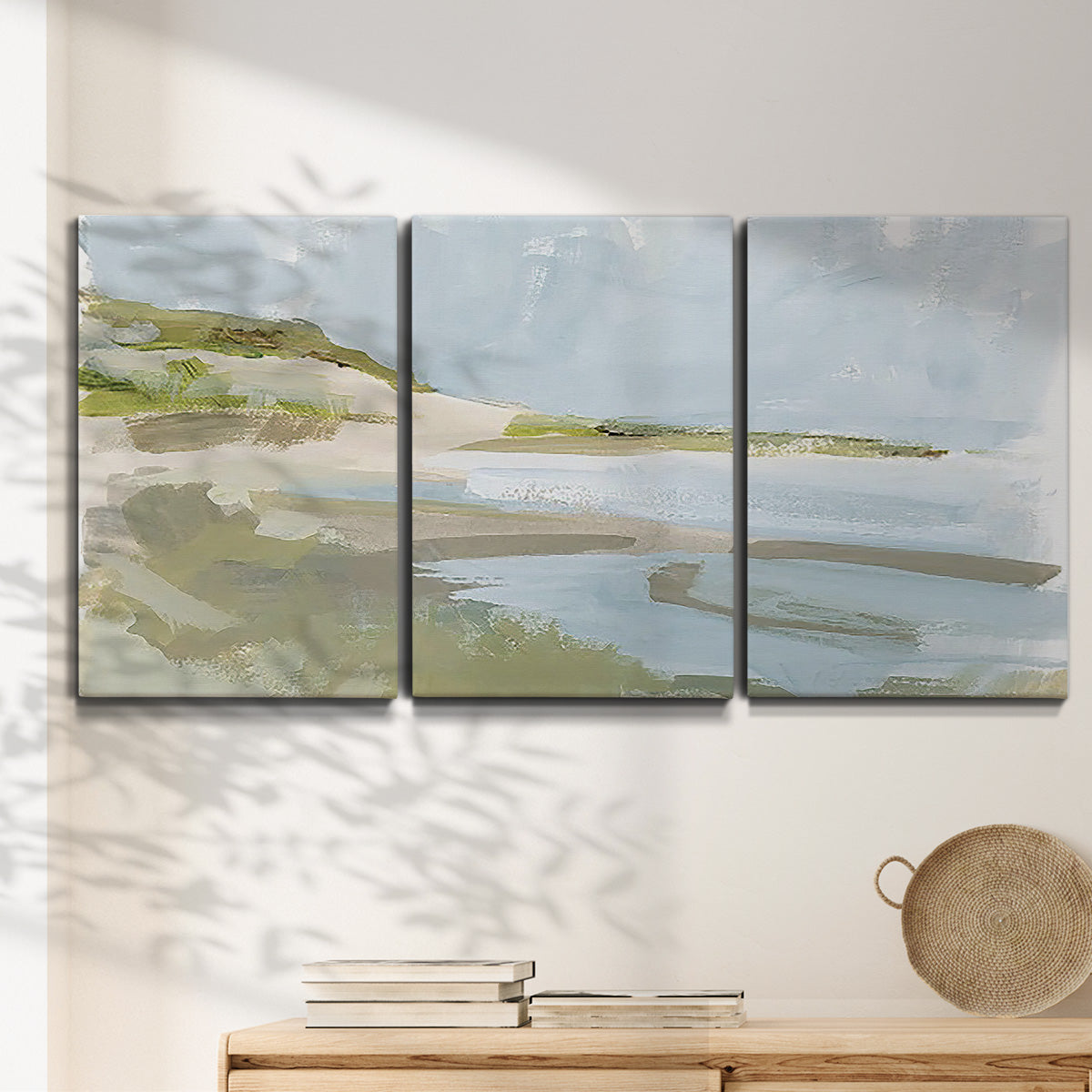 Three-panel canvas wall art featuring coastal cove with calm water, displayed in a minimalist living room above a console table.