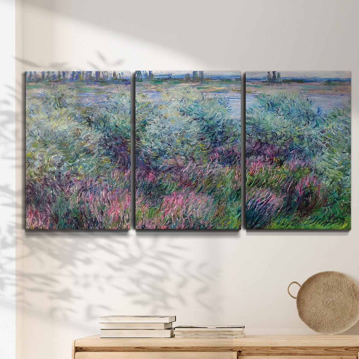 Three-panel canvas wall art featuring flowered riverbank with trees, displayed in a minimalist living room above a console table.