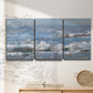 Three-panel canvas wall art featuring overcast coastal waves under grey sky, displayed in a minimalist living room above a console table.