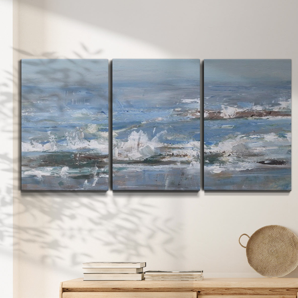 Three-panel canvas wall art featuring overcast coastal waves under grey sky, displayed in a minimalist living room above a console table.