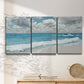 Three-panel canvas wall art featuring tropical beach scene with turquoise water, displayed in a minimalist living room above a console table.
