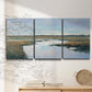 Three-panel canvas wall art featuring coastal plain meeting open water, displayed in a minimalist living room above a console table.