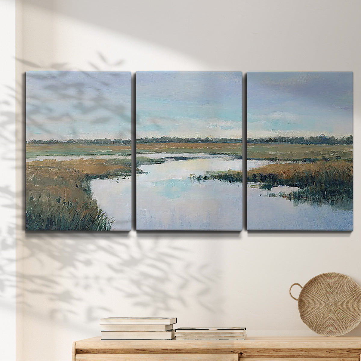 Three-panel canvas wall art featuring coastal plain meeting open water, displayed in a minimalist living room above a console table.