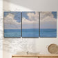 Three-panel canvas wall art featuring coastal shoreline with distant horizon, displayed in a minimalist living room above a console table.