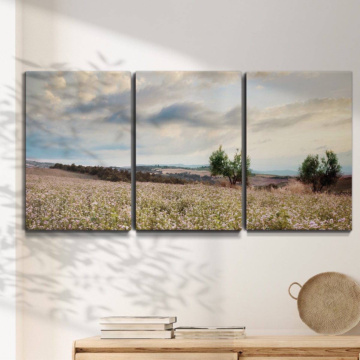 Three-panel canvas wall art featuring wildflowers across tuscan landscape, displayed in a minimalist living room above a console table.