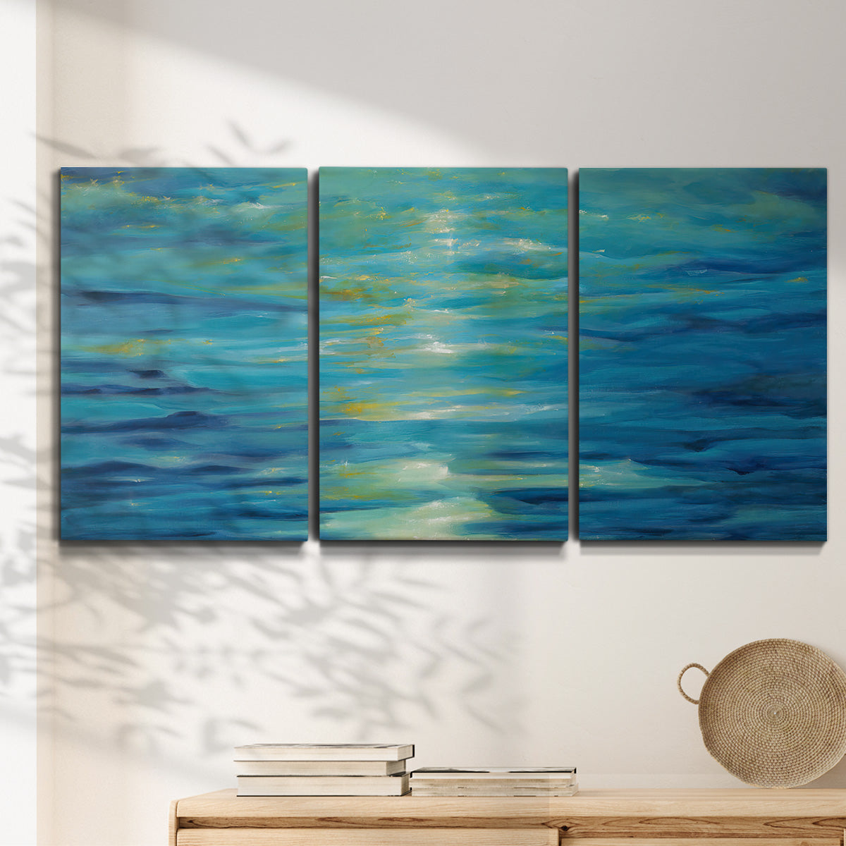 Three-panel canvas wall art featuring deep blue ocean water abstraction, displayed in a minimalist living room above a console table.