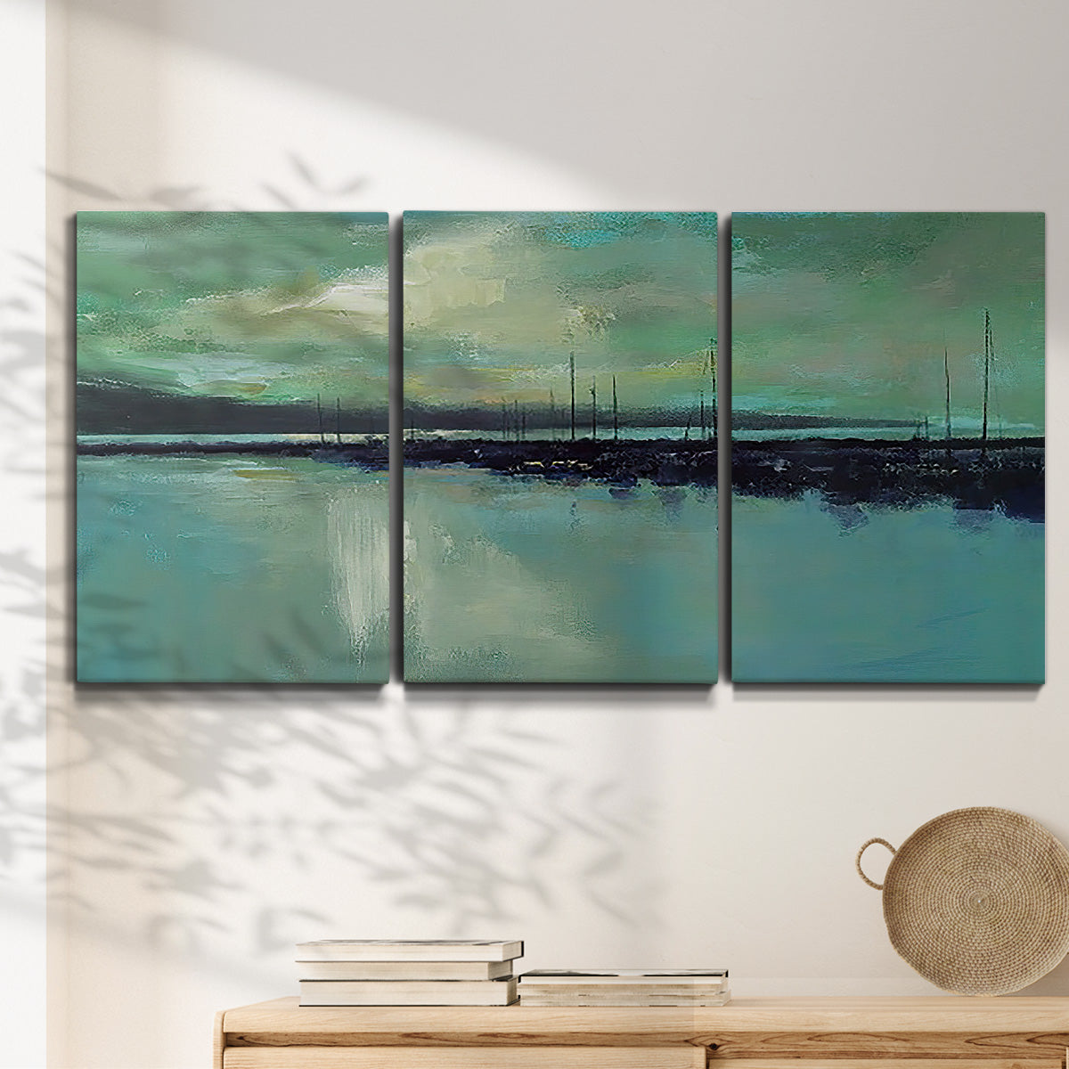 Three-panel canvas wall art featuring calm harbor water with glowing horizon, displayed in a minimalist living room above a console table.