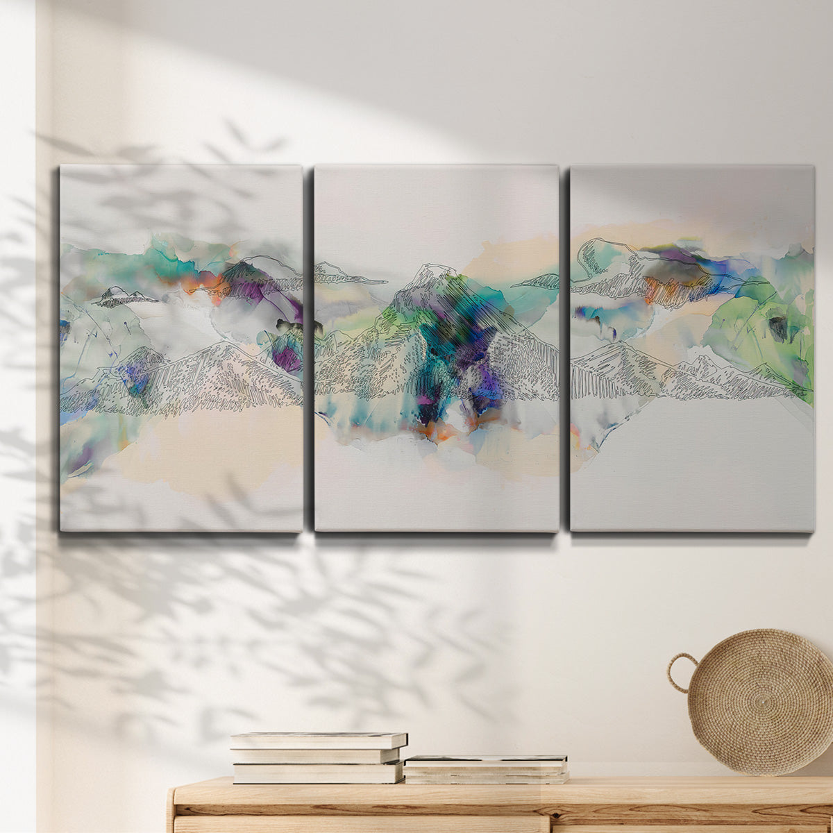 Three-panel canvas wall art featuring abstract mountain range watercolor, displayed in a minimalist living room above a console table.
