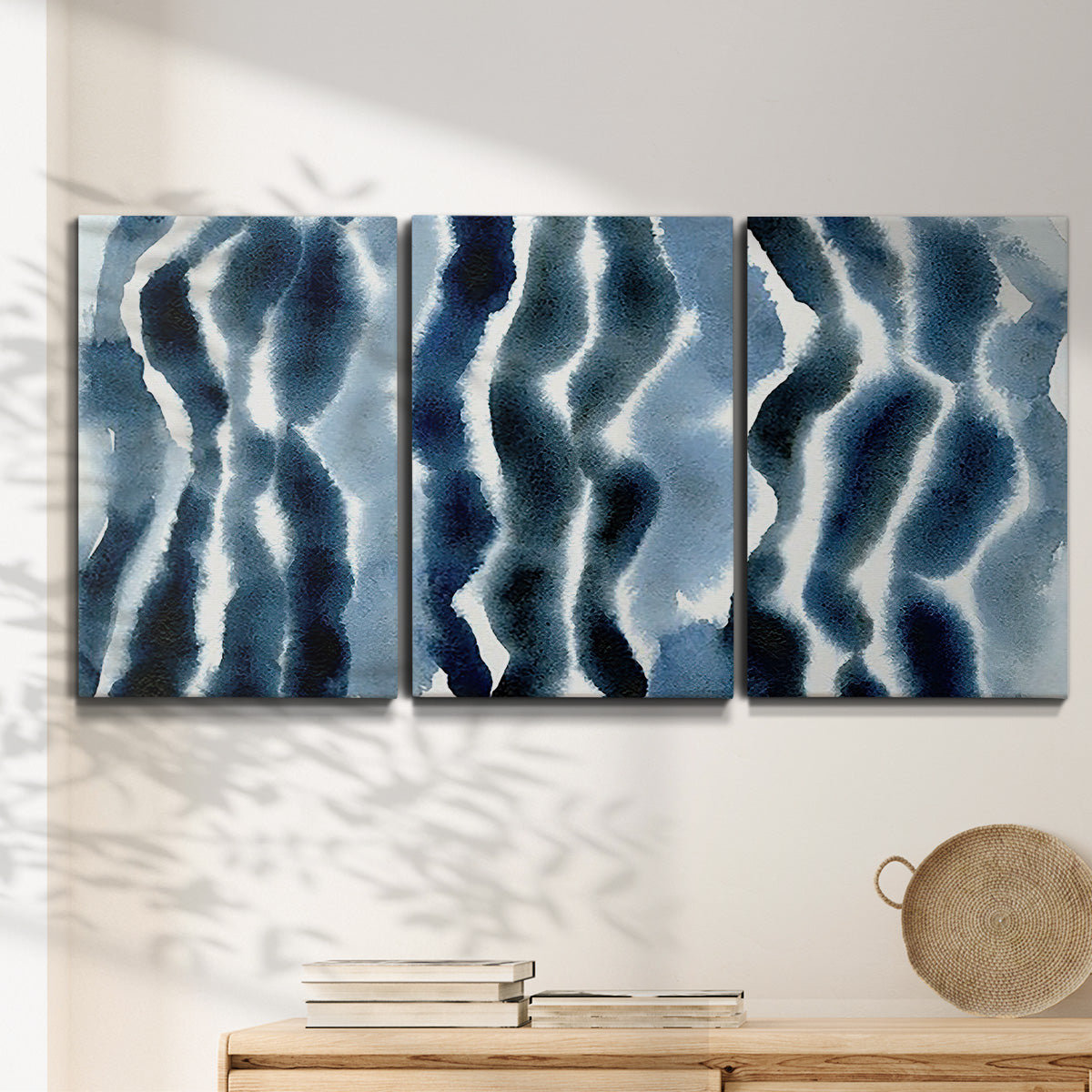 Three-panel canvas wall art featuring flowing blue watercolor wave forms, displayed in a minimalist living room above a console table.