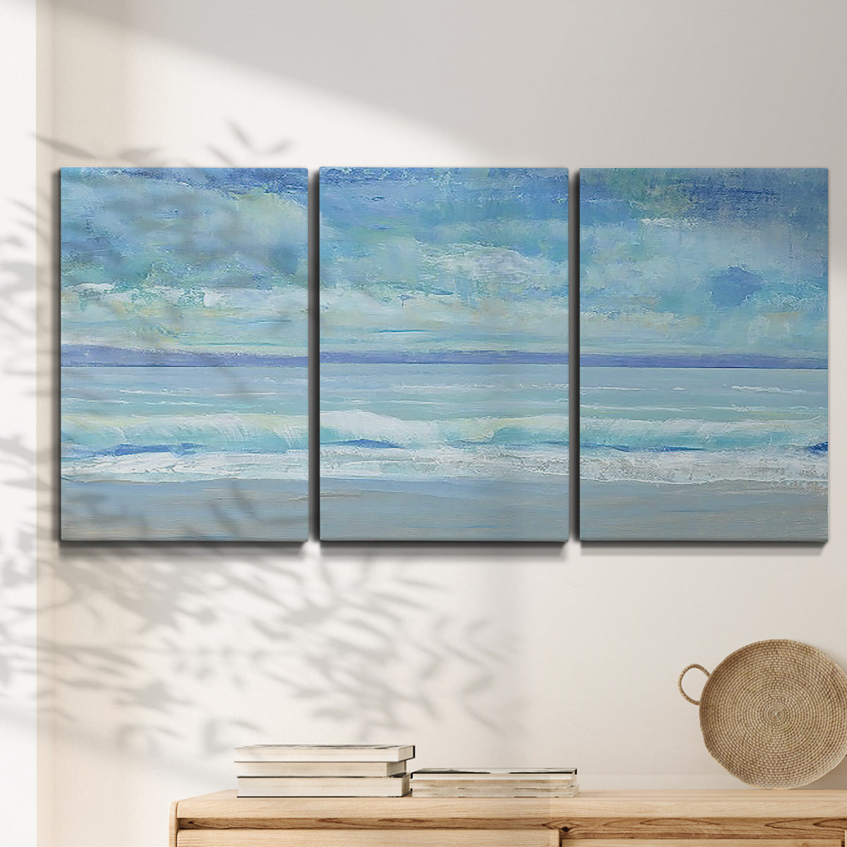 Three-panel canvas wall art featuring rolling ocean surf along shoreline, displayed in a minimalist living room above a console table.