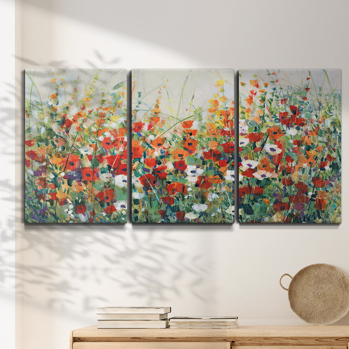Three-panel canvas wall art featuring colorful garden flowers in bloom, displayed in a minimalist living room above a console table.