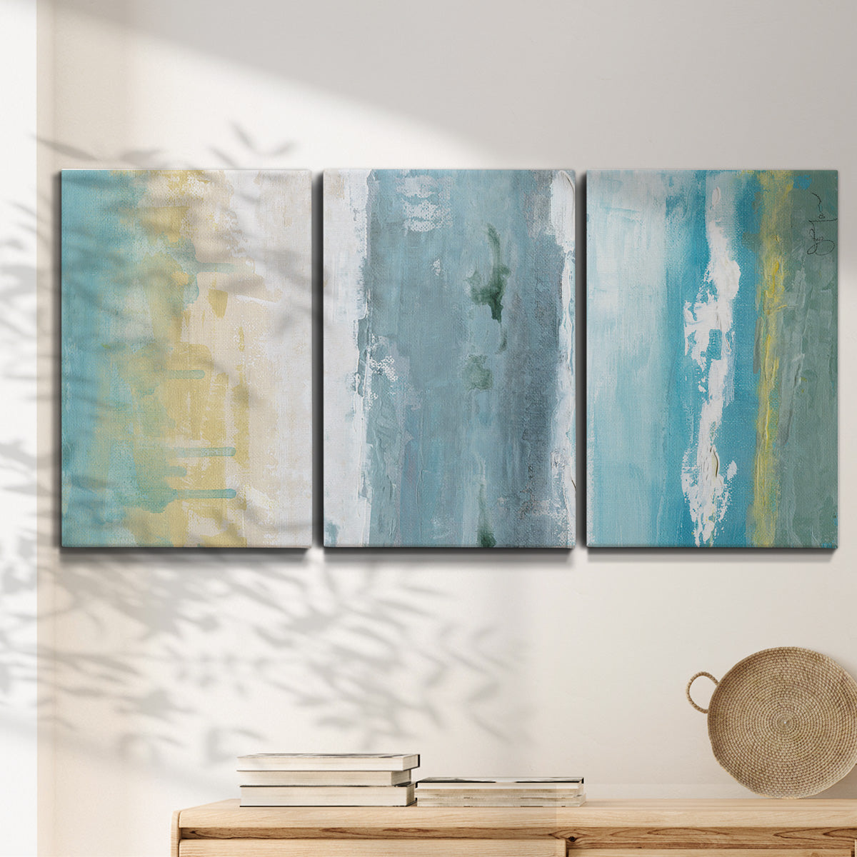 Three-panel canvas wall art featuring abstract coastal shoreline textures, displayed in a minimalist living room above a console table.