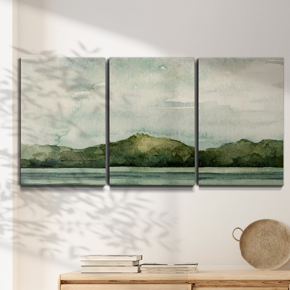 Three-panel canvas wall art featuring riverbank watercolor landscape, displayed in a minimalist living room above a console table.