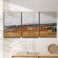 Three-panel canvas wall art featuring abstract bridge landscape in ochre, displayed in a minimalist living room above a console table.