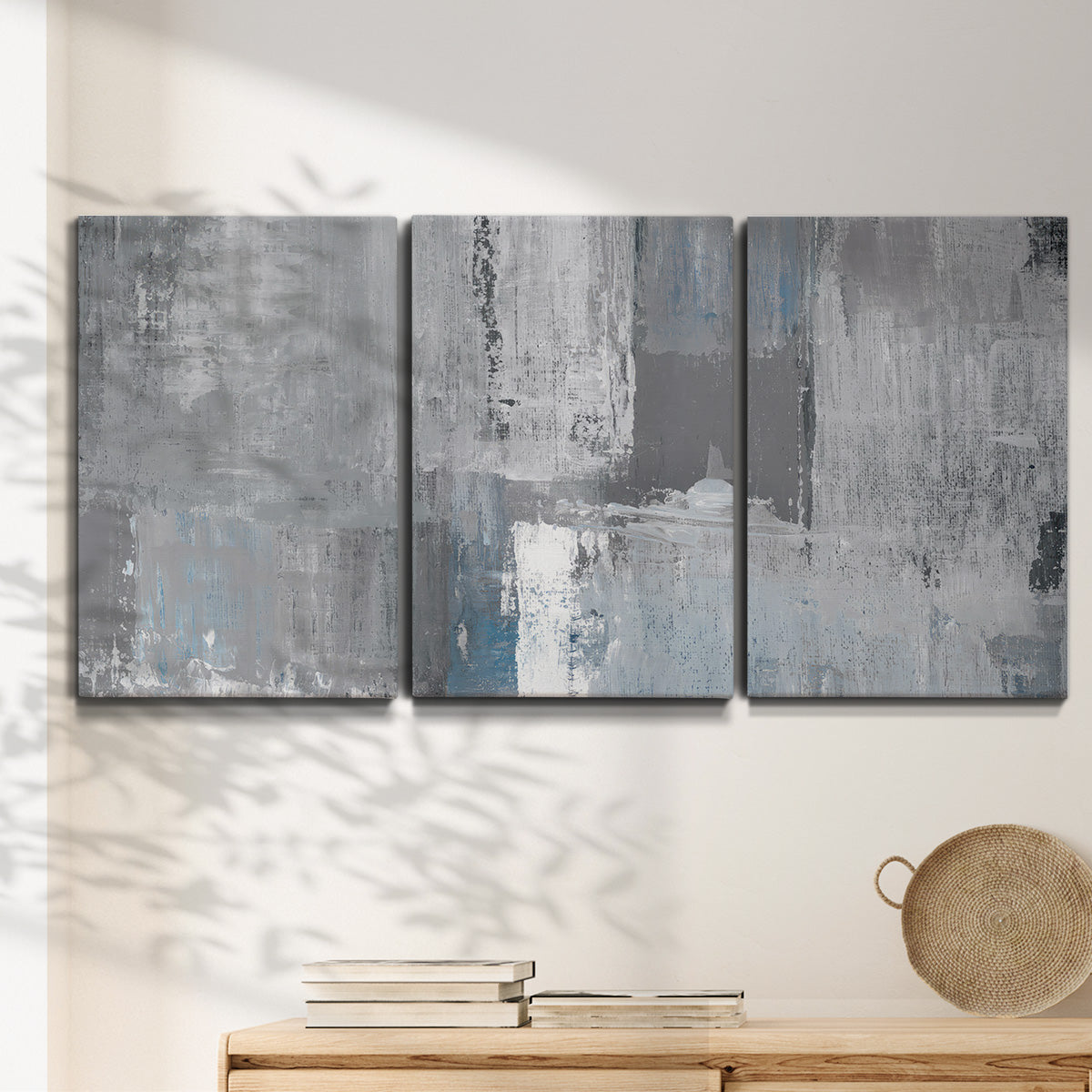 Three-panel canvas wall art featuring cool toned industrial abstract blues, displayed in a minimalist living room above a console table.