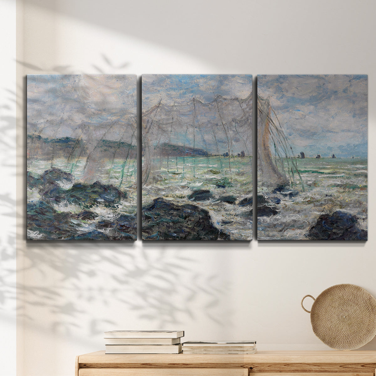 Three-panel canvas wall art featuring rough seas along rocky coast, displayed in a minimalist living room above a console table.