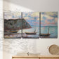 Three-panel canvas wall art featuring golden coastal sunset with cliffs, displayed in a minimalist living room above a console table.