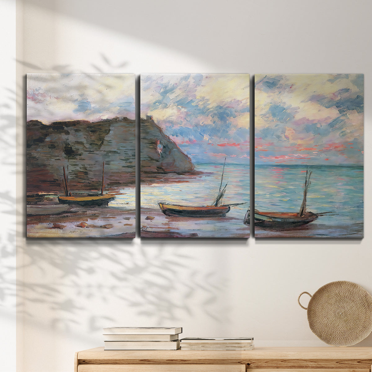 Three-panel canvas wall art featuring golden coastal sunset with cliffs, displayed in a minimalist living room above a console table.