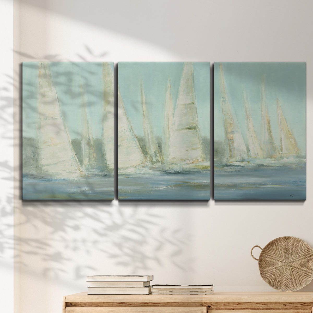Three-panel canvas wall art featuring sailboats silhouetted at sunrise, displayed in a minimalist living room above a console table.