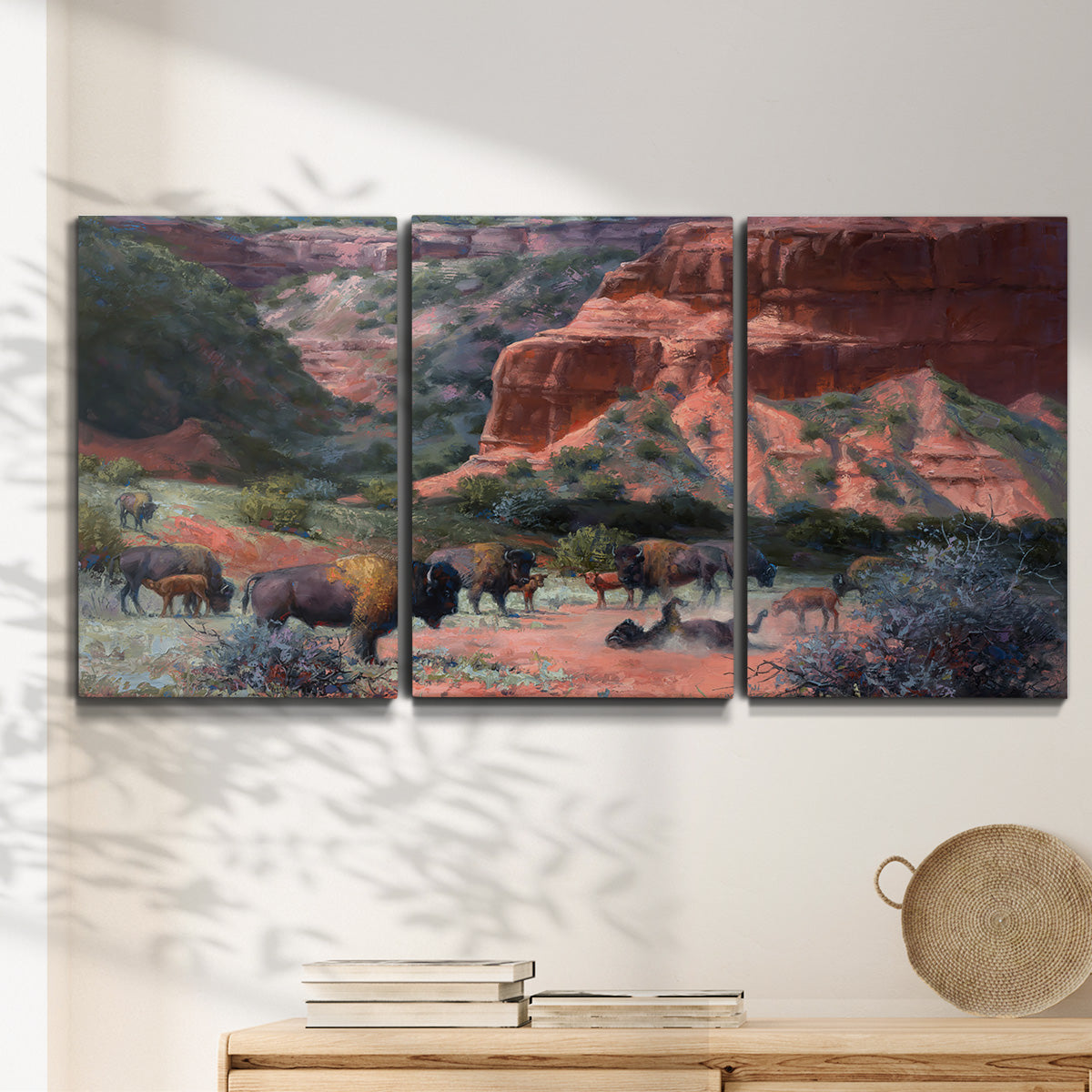 Three-panel canvas wall art featuring rugged canyon landscape with wildlife, displayed in a minimalist living room above a console table.