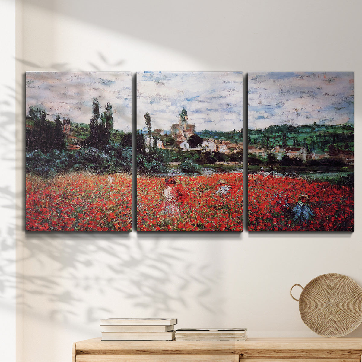 Three-panel canvas wall art featuring poppy field beside village landscape, displayed in a minimalist living room above a console table.