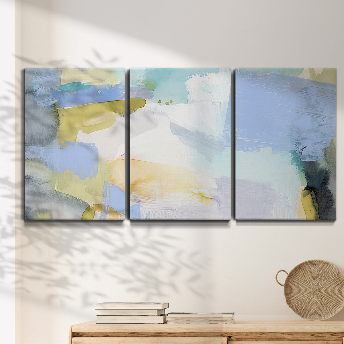 Three-panel canvas wall art featuring soft abstract spring watercolor tones, displayed in a minimalist living room above a console table.