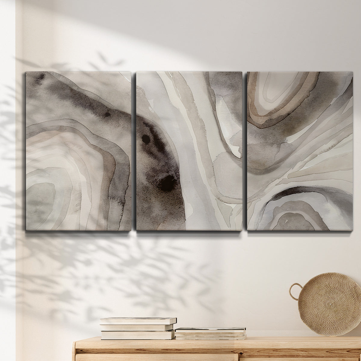 Three-panel canvas wall art featuring layered stone inspired abstract forms, displayed in a minimalist living room above a console table.