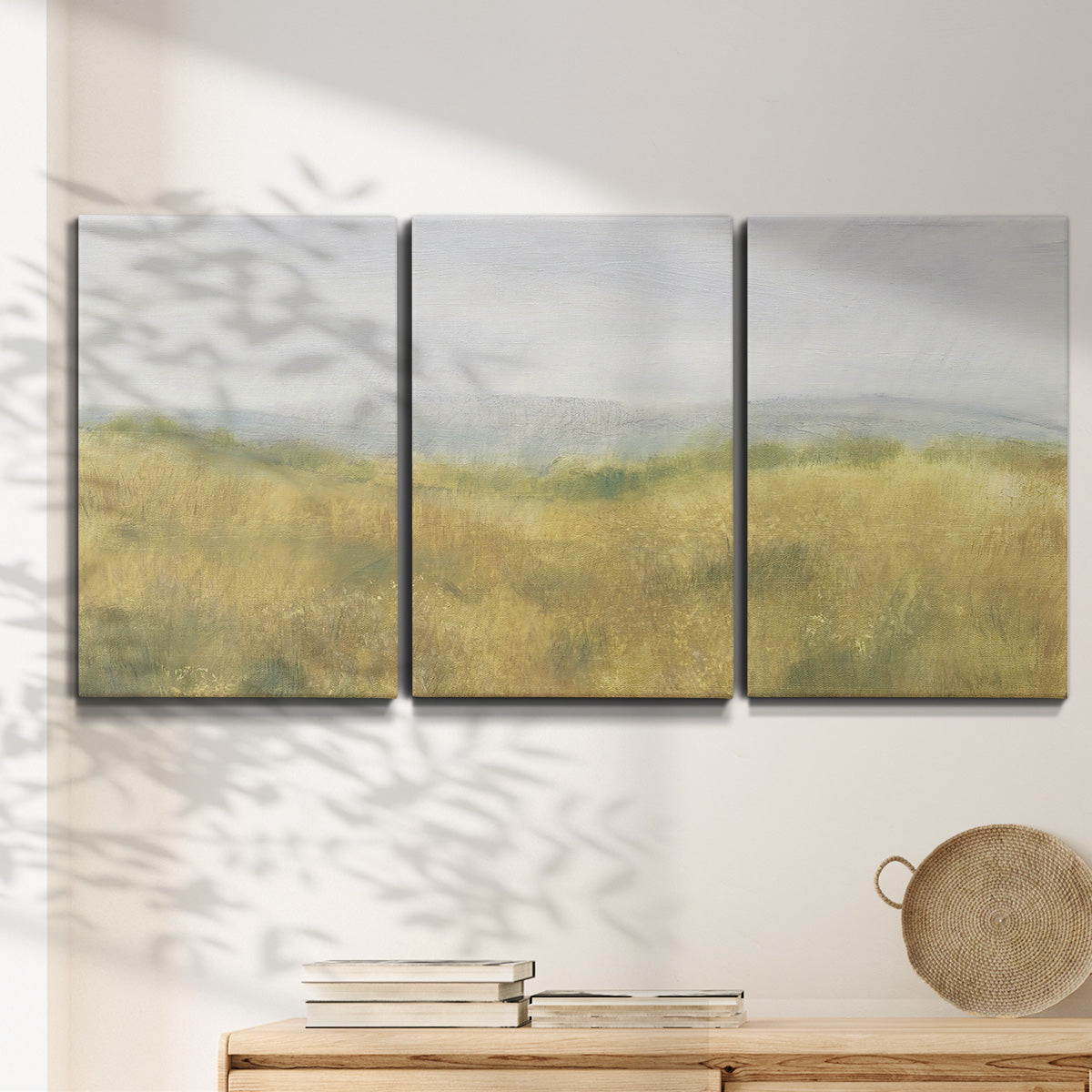 Three-panel canvas wall art featuring pastoral wheat field landscape, displayed in a minimalist living room above a console table.