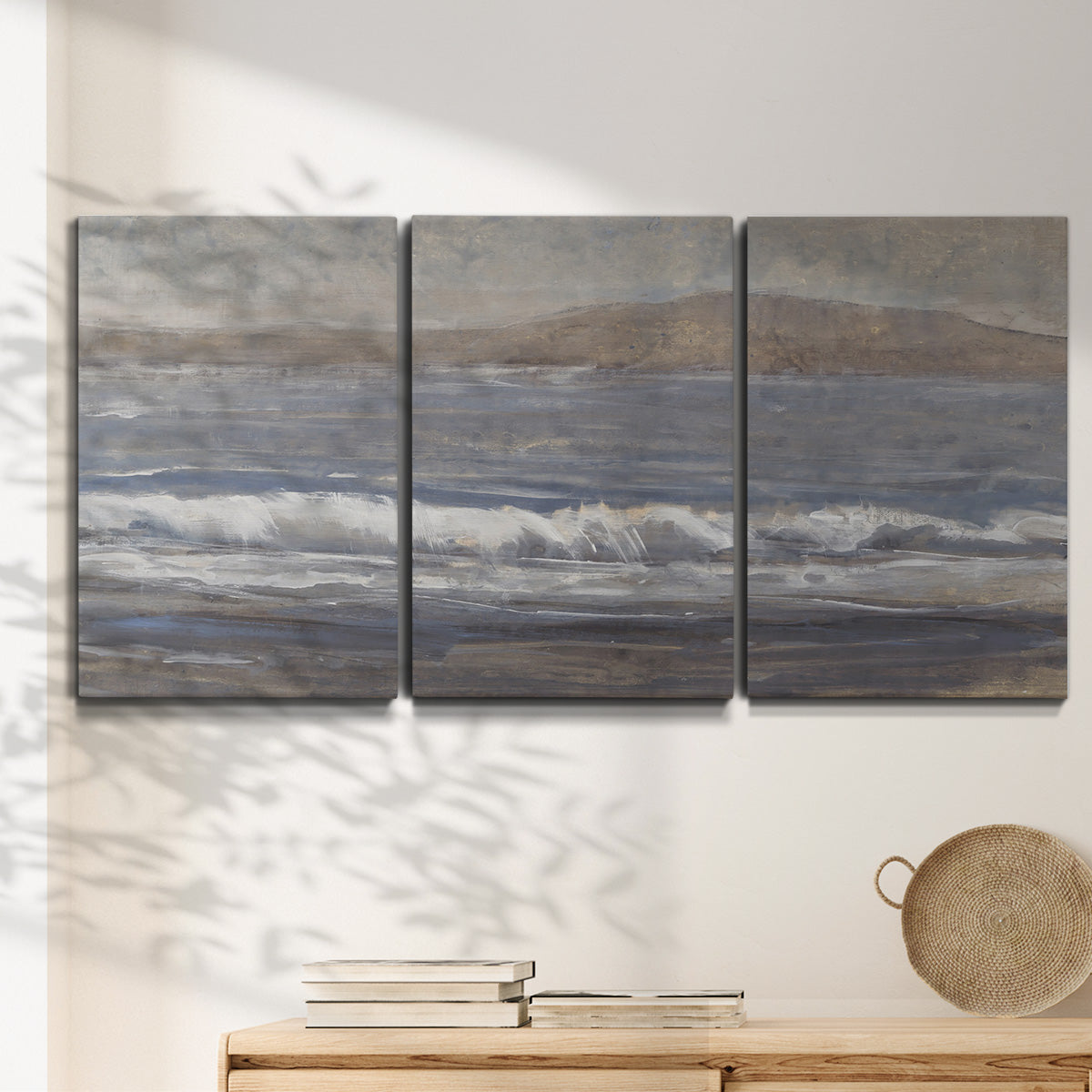 Three-panel canvas wall art featuring shoreline between land and sea, displayed in a minimalist living room above a console table.