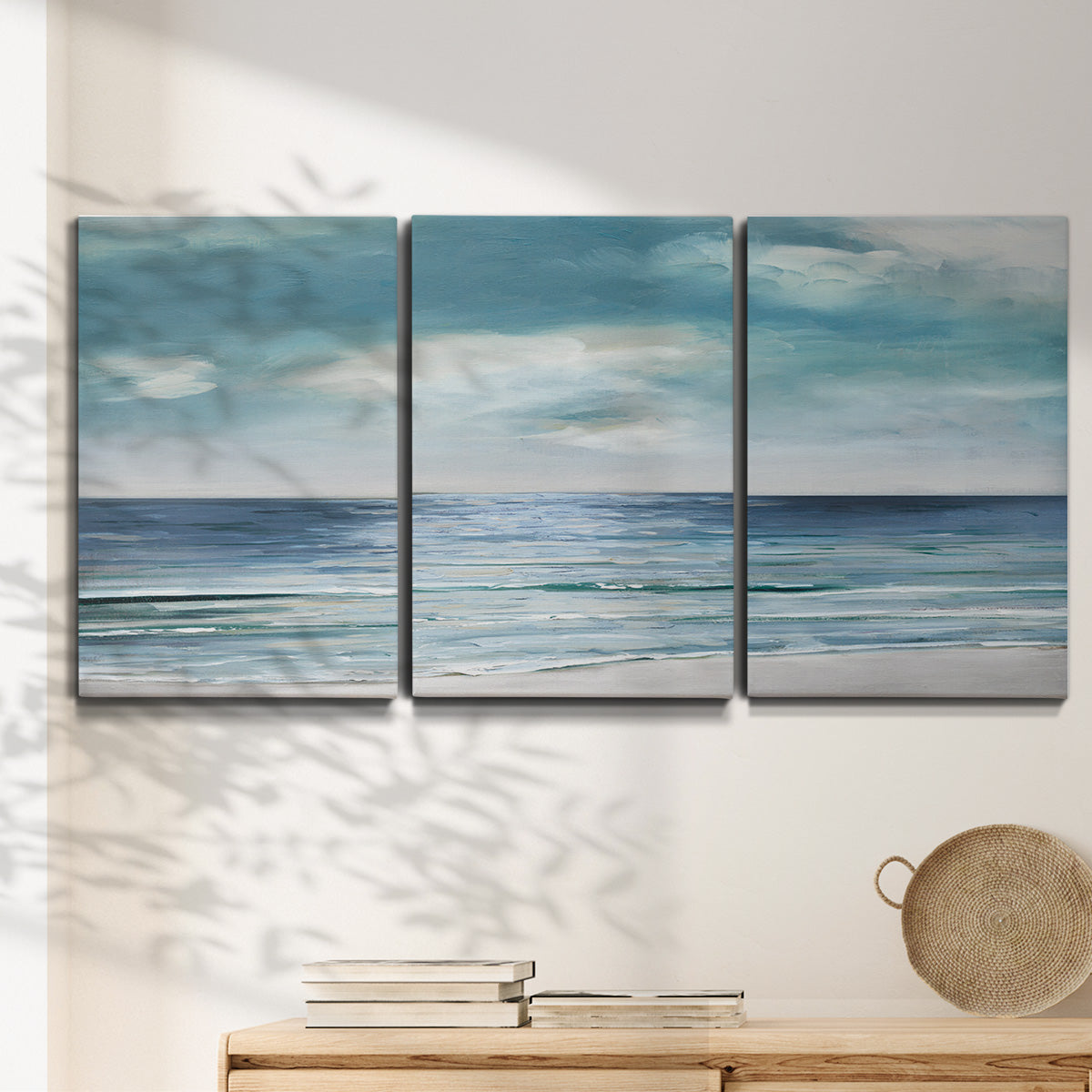 Three-panel canvas wall art featuring calm coastal shoreline, displayed in a minimalist living room above a console table.