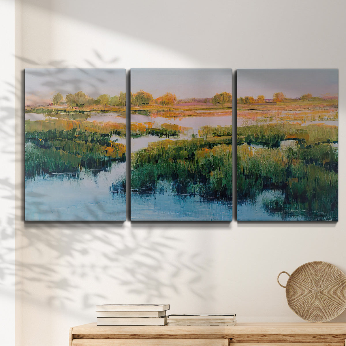Three-panel canvas wall art featuring pastoral marshland landscape, displayed in a minimalist living room above a console table.