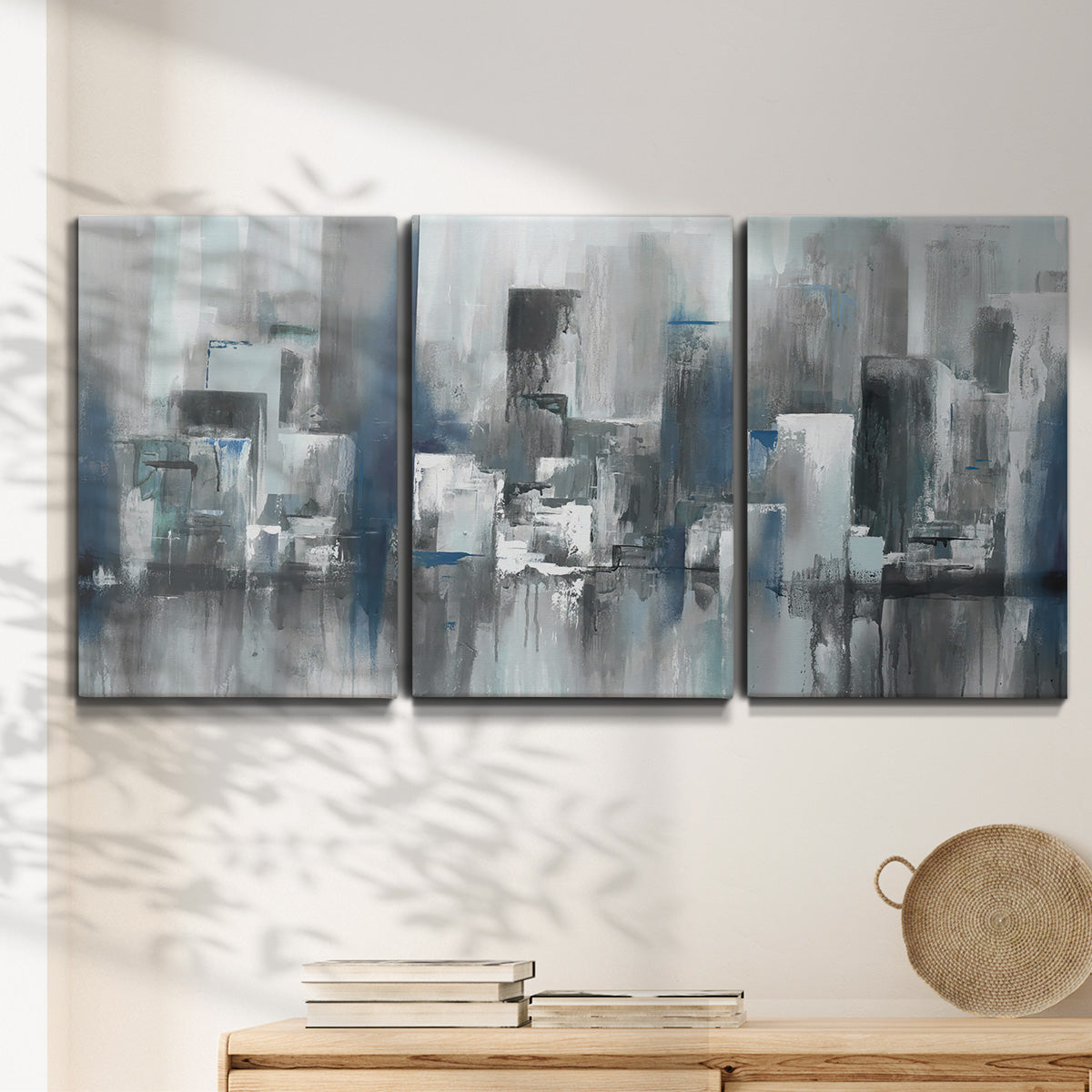 Three-panel canvas wall art featuring urban cityscape rendered in blue tones, displayed in a minimalist living room above a console table.