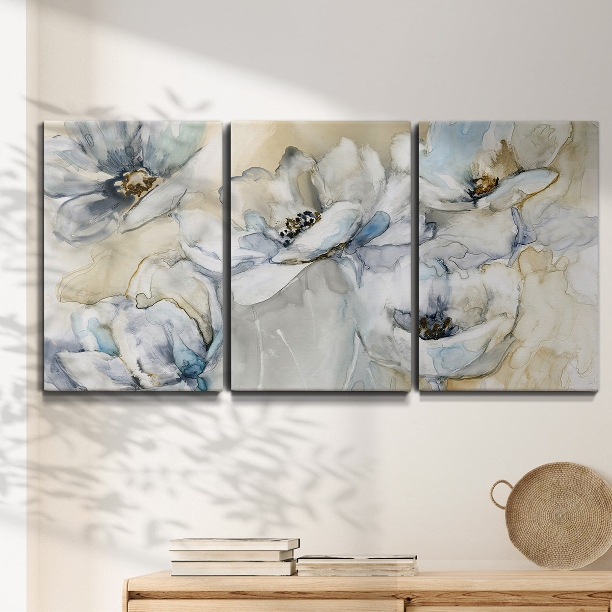 Three-panel canvas wall art featuring delicate watercolor floral blooms, displayed in a minimalist living room above a console table.