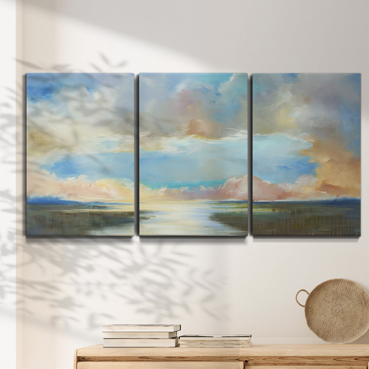 Three-panel canvas wall art featuring dawn light breaking over water, displayed in a minimalist living room above a console table.