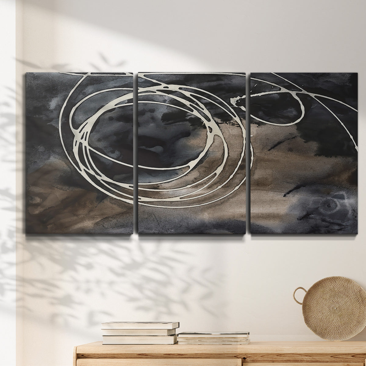 Three-panel canvas wall art featuring dark swirling abstract motion, displayed in a minimalist living room above a console table.