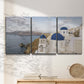 Three-panel canvas wall art featuring white buildings overlooking sea cliffs, displayed in a minimalist living room above a console table.