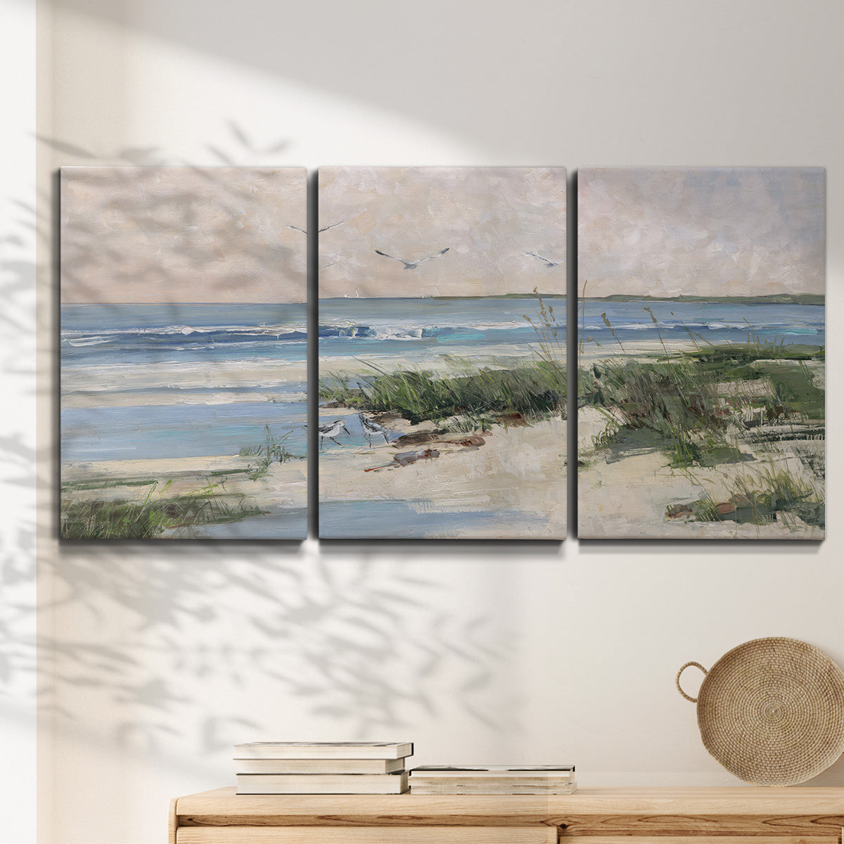 Three-panel canvas wall art featuring soft morning light over calm sea, displayed in a minimalist living room above a console table.