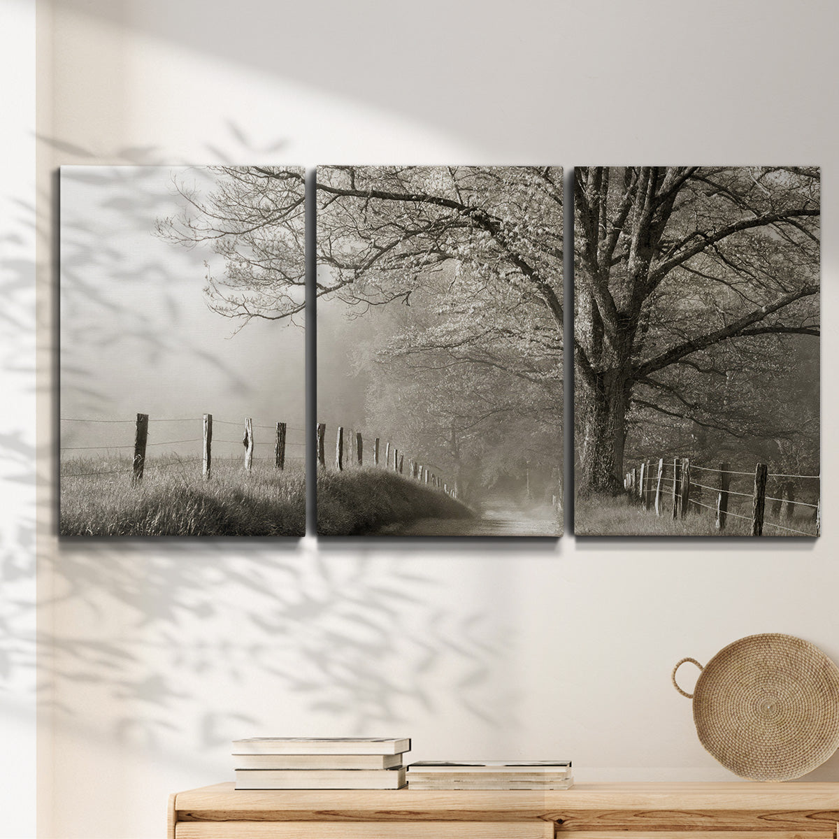Three-panel canvas wall art featuring fenced rural path through countryside, displayed in a minimalist living room above a console table.