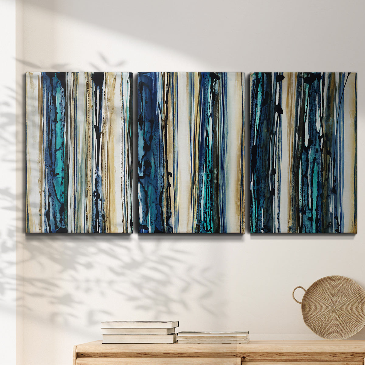 Three-panel canvas wall art featuring vertical blue abstract streaks, displayed in a minimalist living room above a console table.