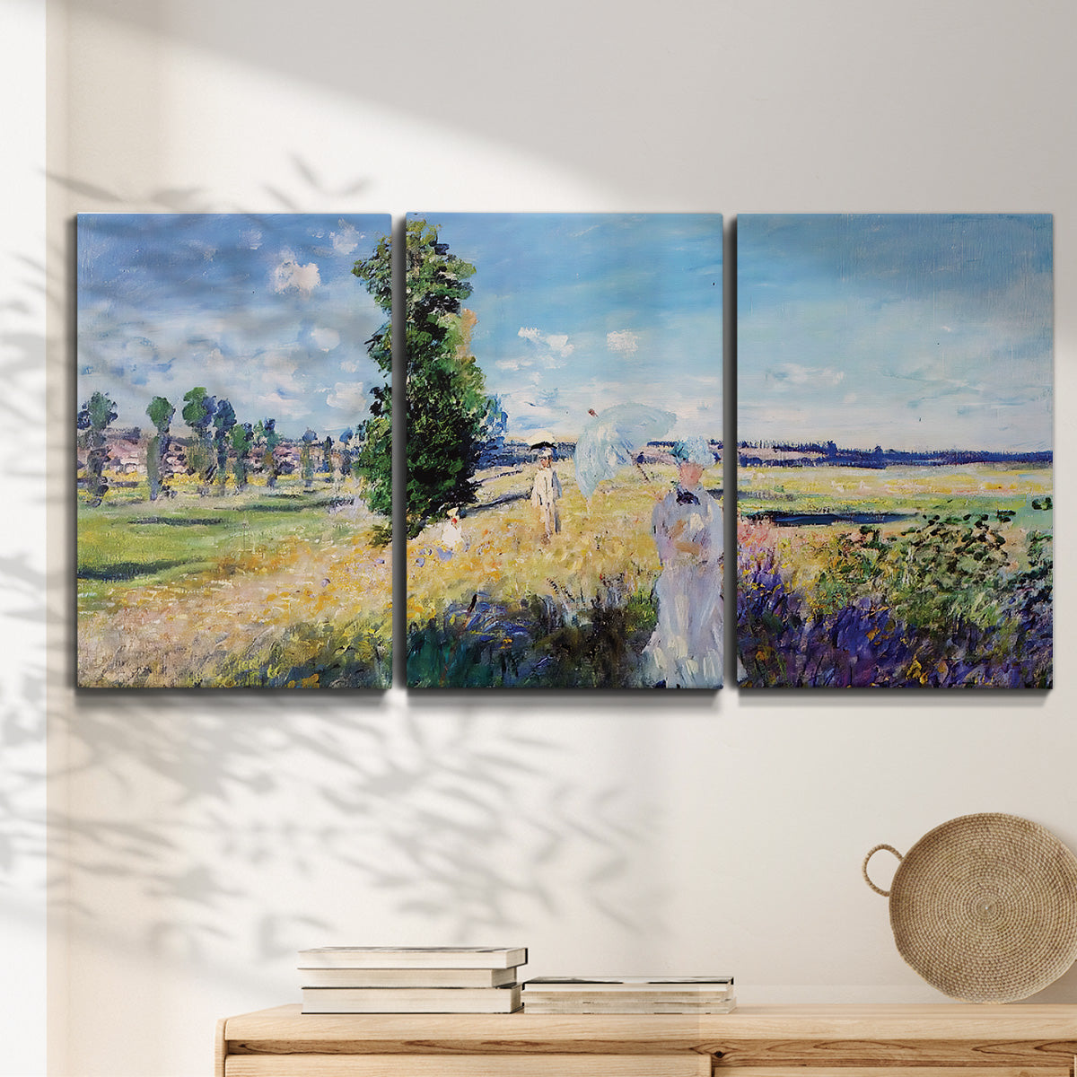 Three-panel canvas wall art featuring riverside path with figures, displayed in a minimalist living room above a console table.