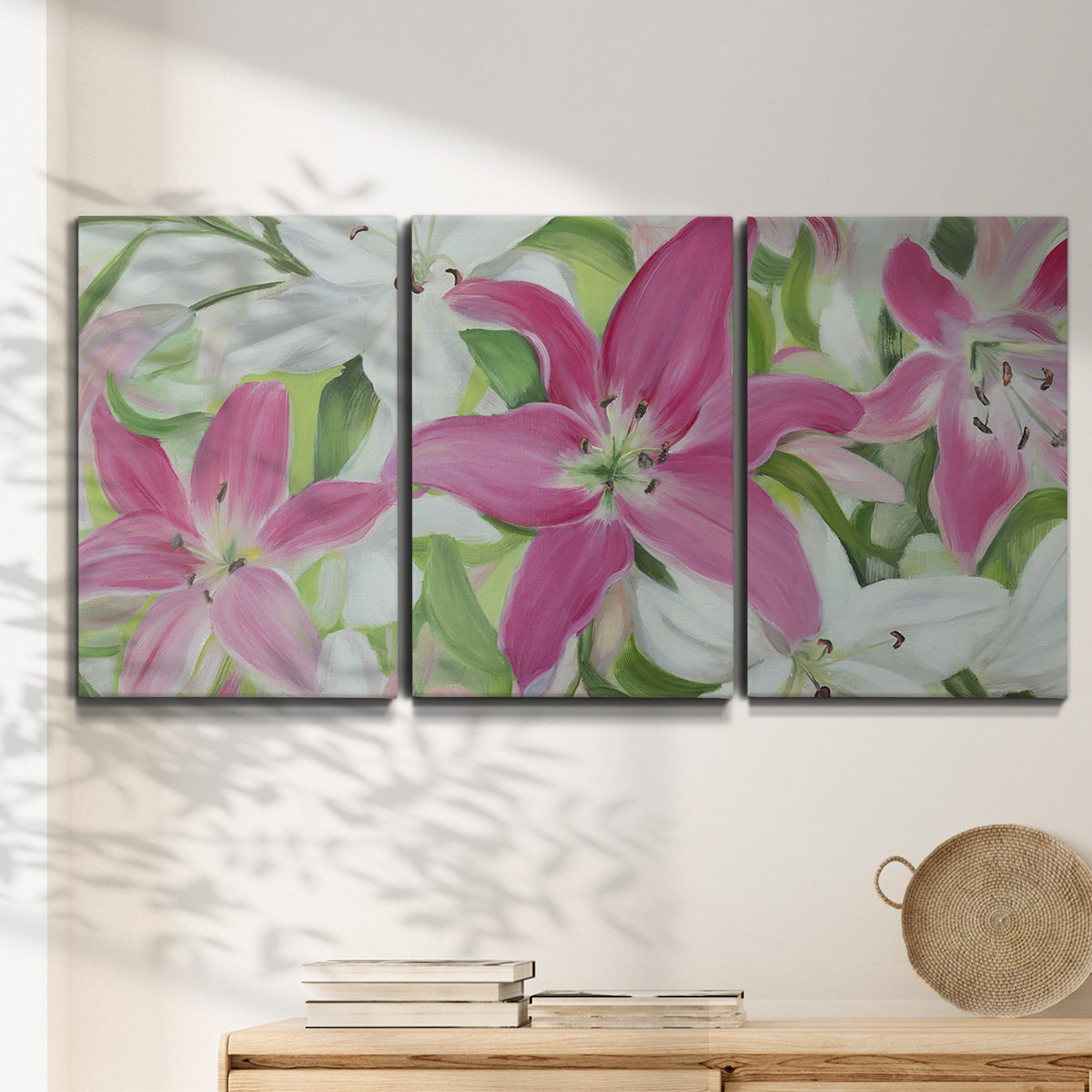 Three-panel canvas wall art featuring pink and white lilies in bloom, displayed in a minimalist living room above a console table.