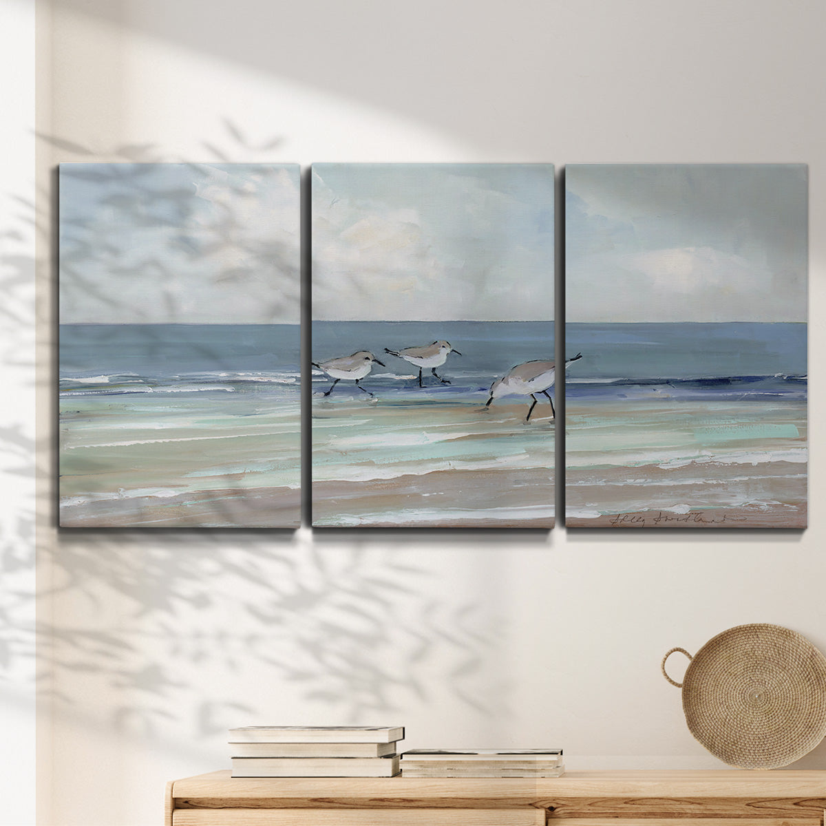 Three-panel canvas wall art featuring shore birds searching along beach, displayed in a minimalist living room above a console table.