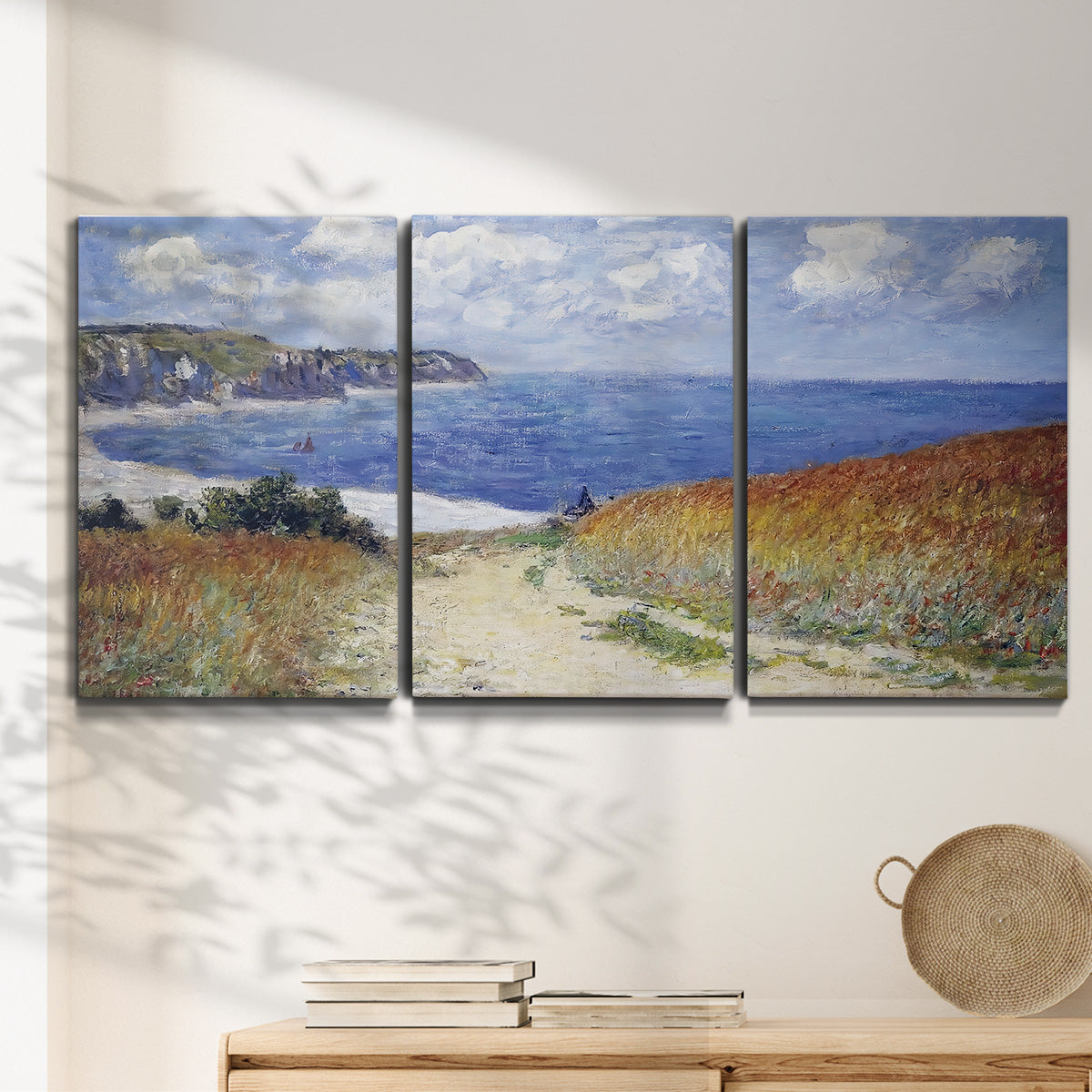 Three-panel canvas wall art featuring coastal path leading to sea, displayed in a minimalist living room above a console table.
