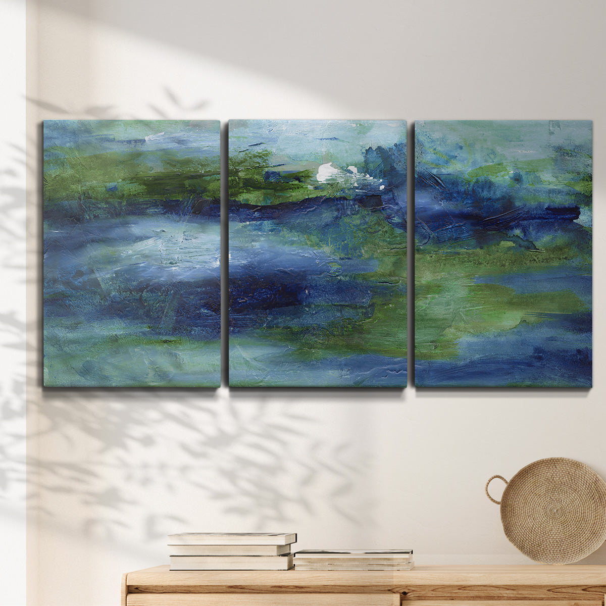 Three-panel canvas wall art featuring flowing blue abstract watercolor, displayed in a minimalist living room above a console table.