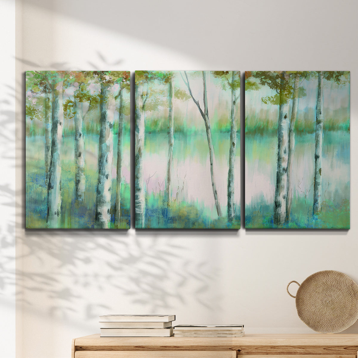 Three-panel canvas wall art featuring calm lake framed by aspen trees, displayed in a minimalist living room above a console table.