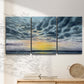 Three-panel canvas wall art featuring tropical coastal sunset over water, displayed in a minimalist living room above a console table.