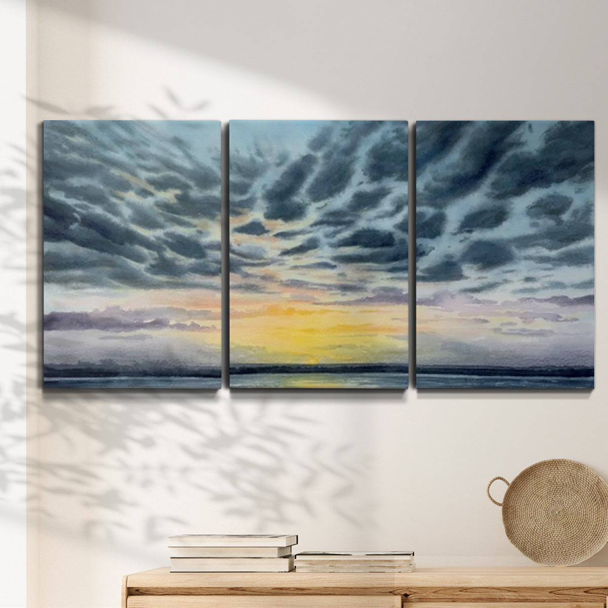 Three-panel canvas wall art featuring tropical coastal sunset over water, displayed in a minimalist living room above a console table.