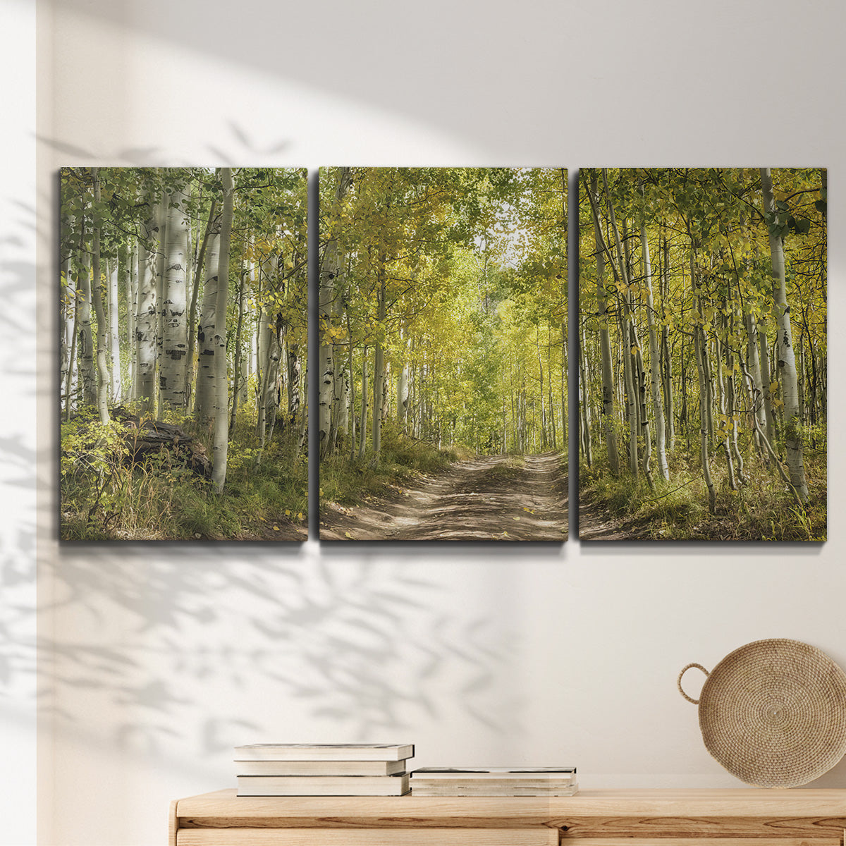 Three-panel canvas wall art featuring tree lined forest road photograph, displayed in a minimalist living room above a console table.