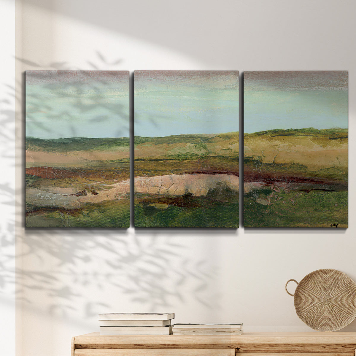 Three-panel canvas wall art featuring pastoral landscape with winding road, displayed in a minimalist living room above a console table.