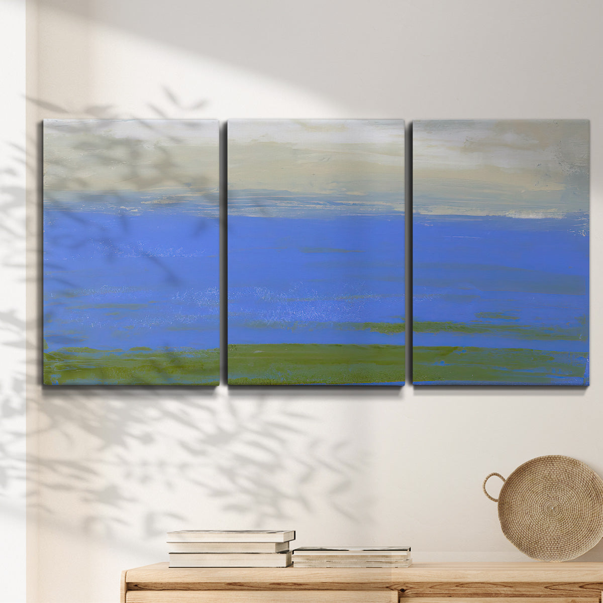 Three-panel canvas wall art featuring abstract coastal inlet landscape, displayed in a minimalist living room above a console table.